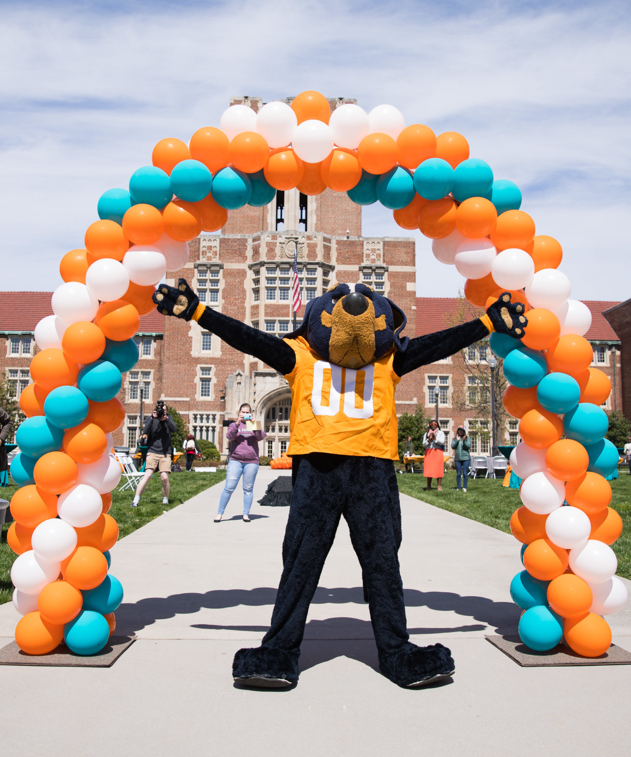 Smokey standing in front of a building with orange, blue and white balloons 